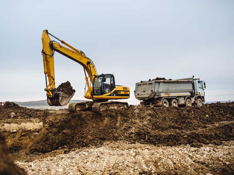 Loader and excavator working in rough terrain to illustrate choosing the best for the job.